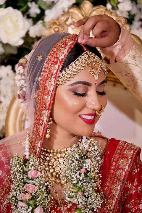 A bride smiling while her dupatta is adjusted