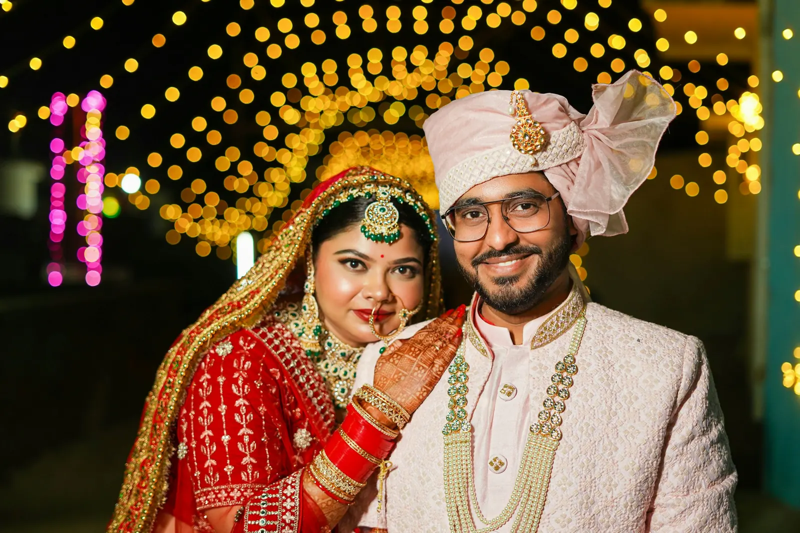 A bride and groom smiling at each other under warm strings of light