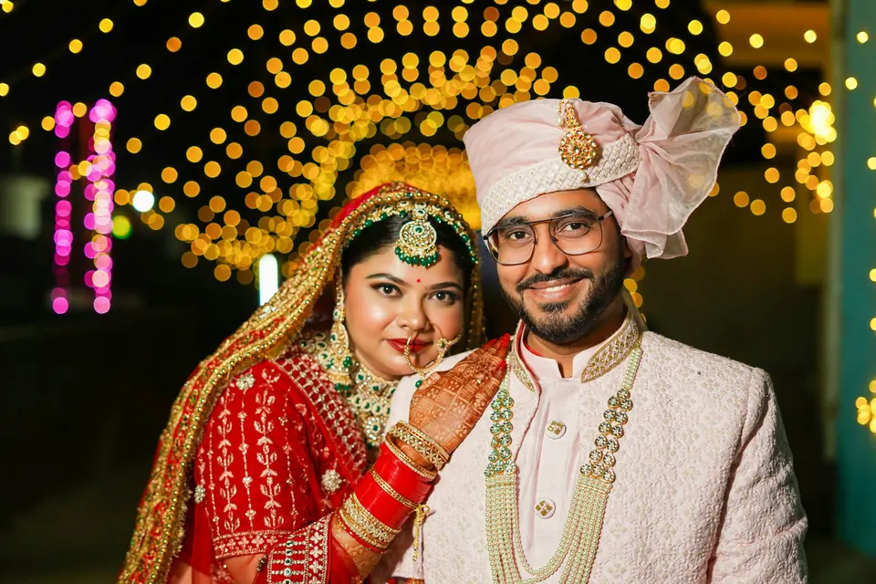 A couple in wedding clothes smiling under strings of warm lights