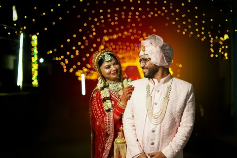 The couple standing together at night, lights glowing behind them
