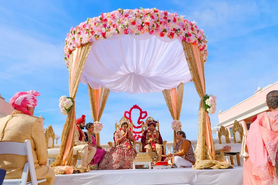 A couple seated under a floral mandap during their wedding ceremony