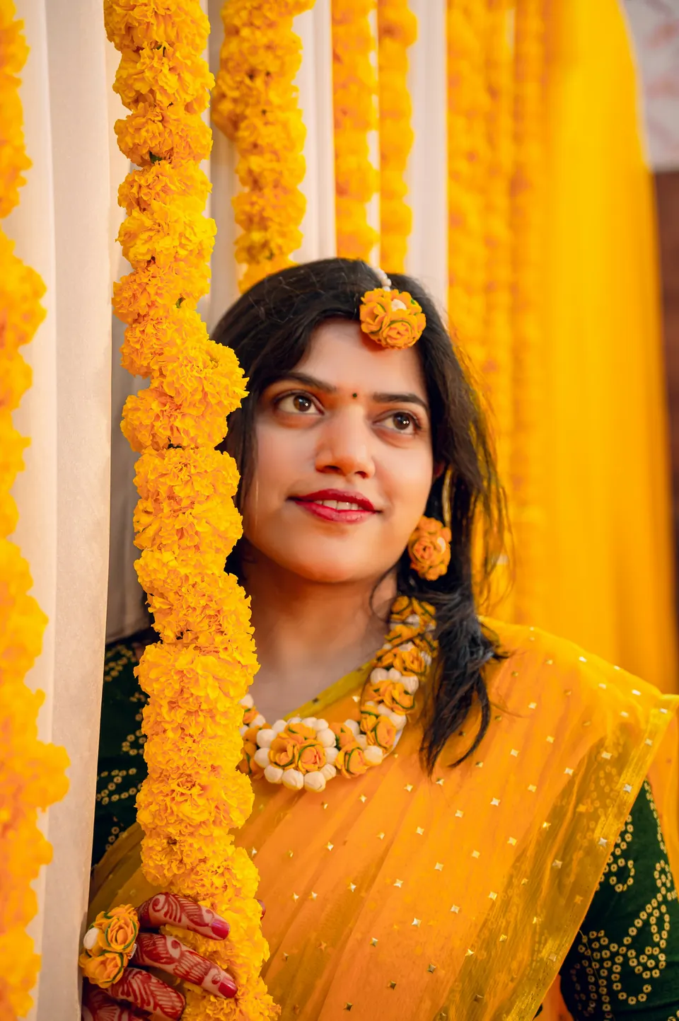 A woman in a yellow sari framed by strings of marigold flowers