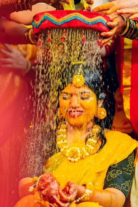 A bride laughing as family pour haldi and water over her