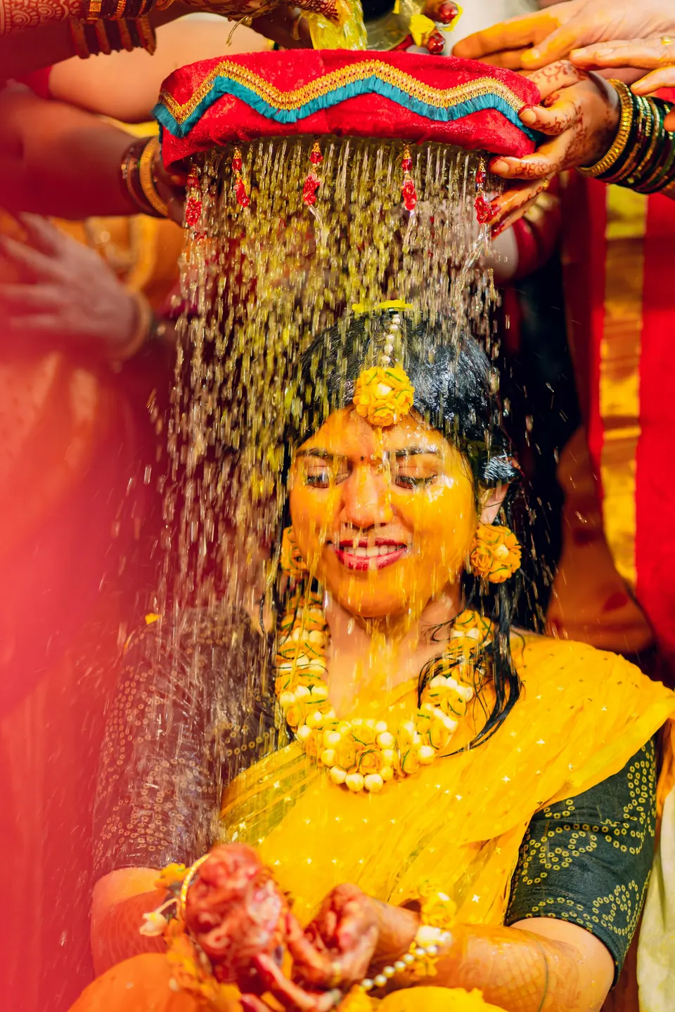 A bride laughing as family pour haldi and water over her head