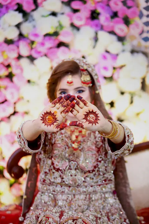 A bride holding up hennaed hands in a heart shape