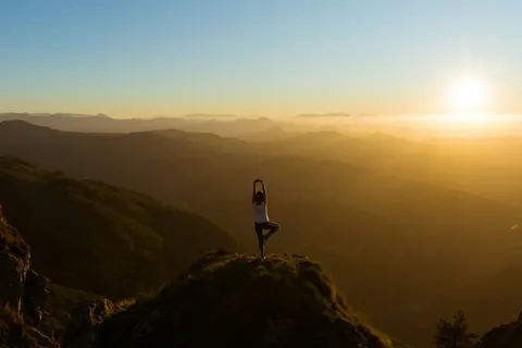 A person on a hilltop at sunset over layered hills