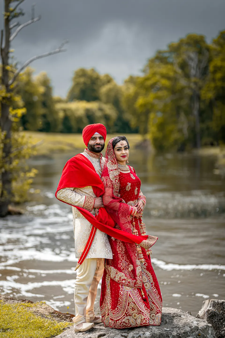 A couple in wedding clothes standing on rocks beside a river